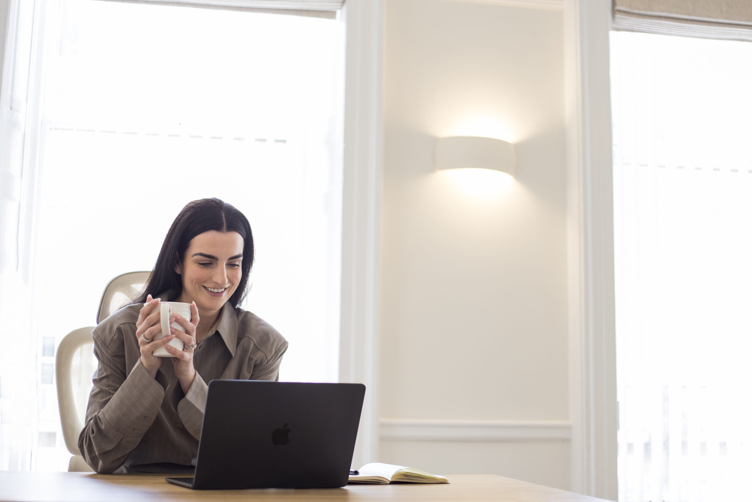 Therapist holding cup of tea whilst doing virtual therapy session on laptop